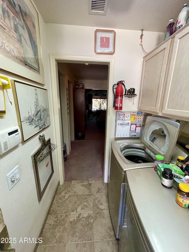 clothes washing area with separate washer and dryer, cabinet space, and visible vents