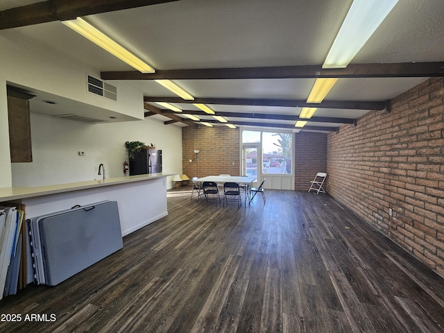 kitchen with brick wall, black fridge, dark hardwood / wood-style floors, and beamed ceiling