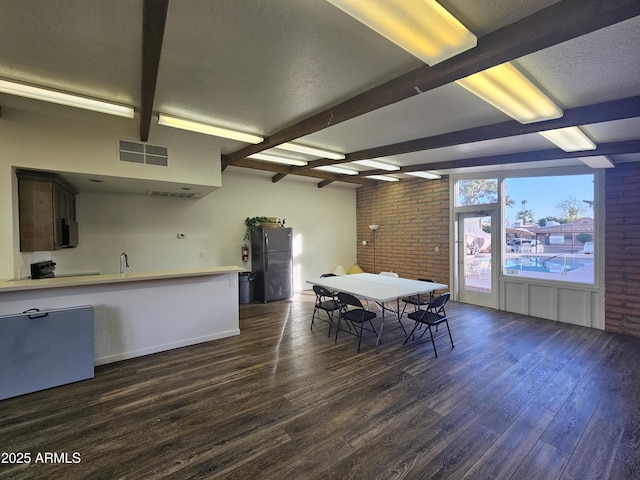 dining room with brick wall, dark hardwood / wood-style floors, and beam ceiling