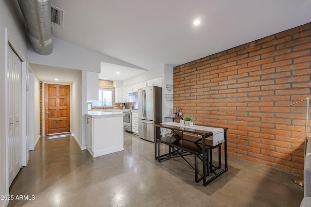 kitchen with stainless steel appliances, brick wall, white cabinets, a kitchen island, and vaulted ceiling