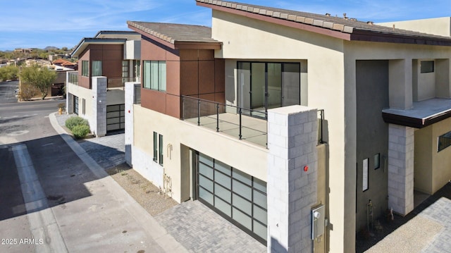 view of side of property with a garage, stucco siding, a balcony, and driveway