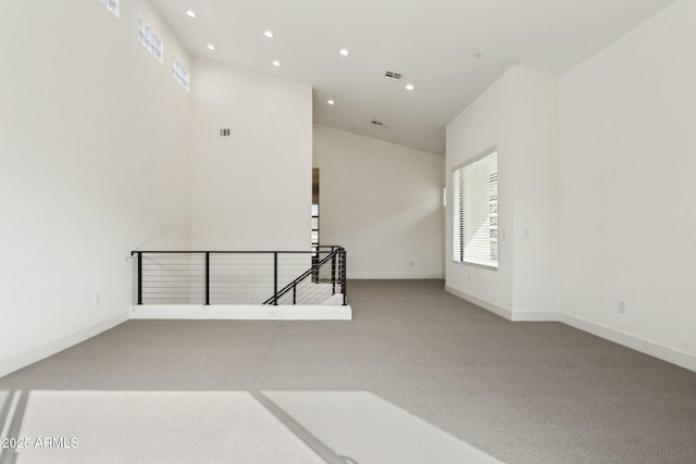 carpeted spare room with recessed lighting, baseboards, a high ceiling, and visible vents