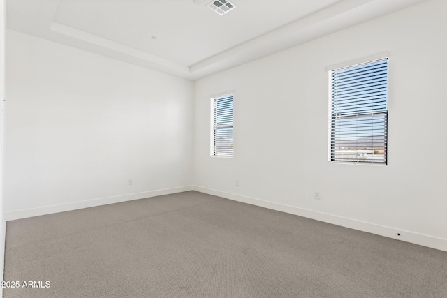 carpeted empty room featuring baseboards, a tray ceiling, and visible vents