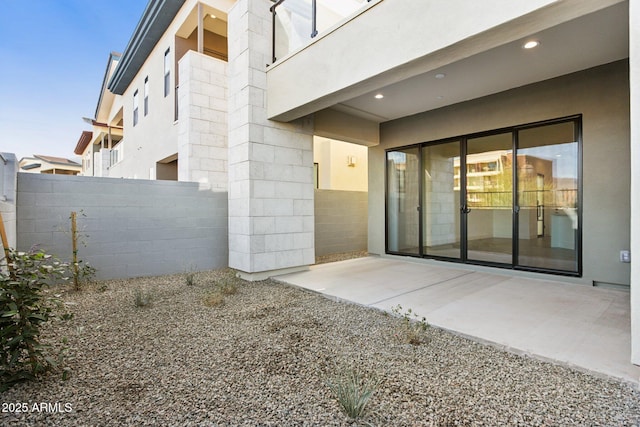 doorway to property with a patio, concrete block siding, fence, and stucco siding