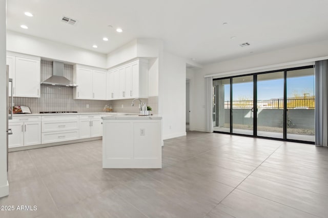 kitchen featuring a sink, wall chimney exhaust hood, white cabinetry, decorative backsplash, and stovetop