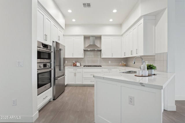 kitchen with visible vents, appliances with stainless steel finishes, a sink, a peninsula, and wall chimney exhaust hood