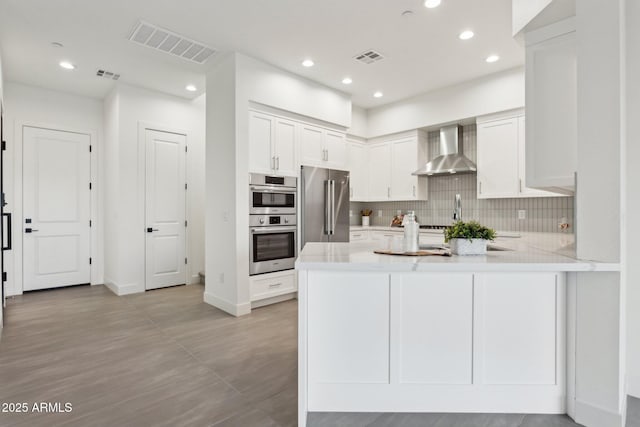 kitchen with visible vents, decorative backsplash, wall chimney exhaust hood, and stainless steel appliances