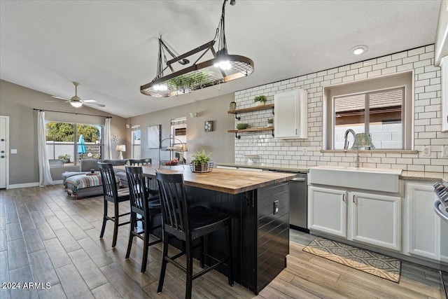 kitchen with a kitchen island, butcher block countertops, backsplash, lofted ceiling, and white cabinets