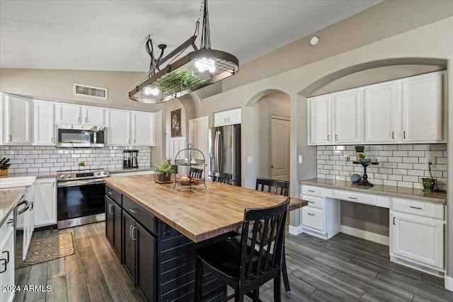 kitchen featuring lofted ceiling, white cabinets, appliances with stainless steel finishes, a kitchen island, and butcher block counters