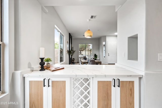 kitchen featuring light stone counters, visible vents, and decorative light fixtures