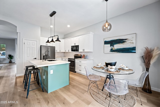 kitchen featuring tasteful backsplash, light countertops, an island with sink, stainless steel appliances, and white cabinetry