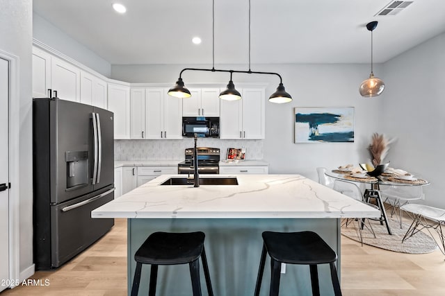 kitchen featuring visible vents, a sink, stainless steel appliances, light wood-type flooring, and backsplash