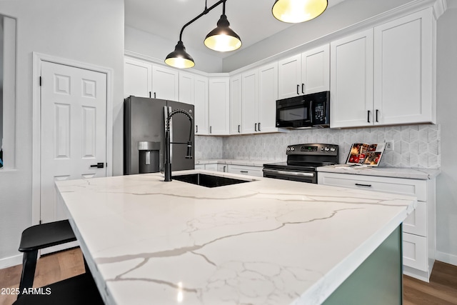 kitchen with black microwave, a center island with sink, fridge with ice dispenser, decorative backsplash, and stainless steel range with electric stovetop