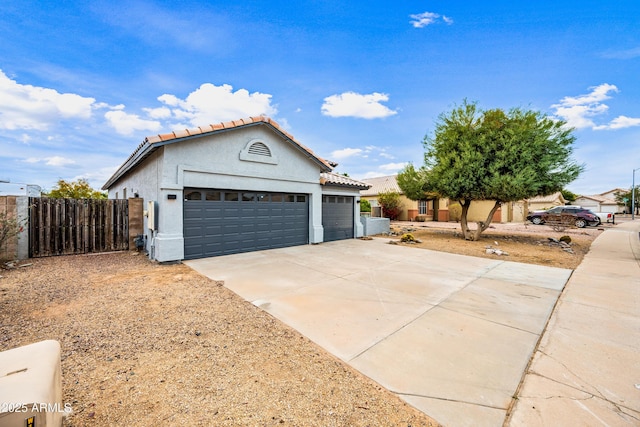 view of front facade with fence, an attached garage, stucco siding, concrete driveway, and a tiled roof