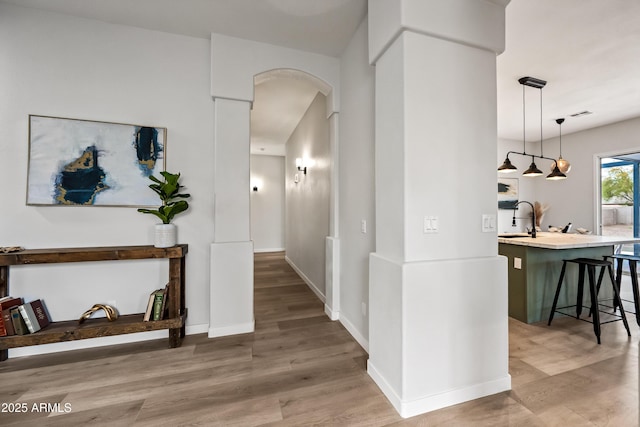 corridor featuring a sink, light wood-style floors, arched walkways, and baseboards