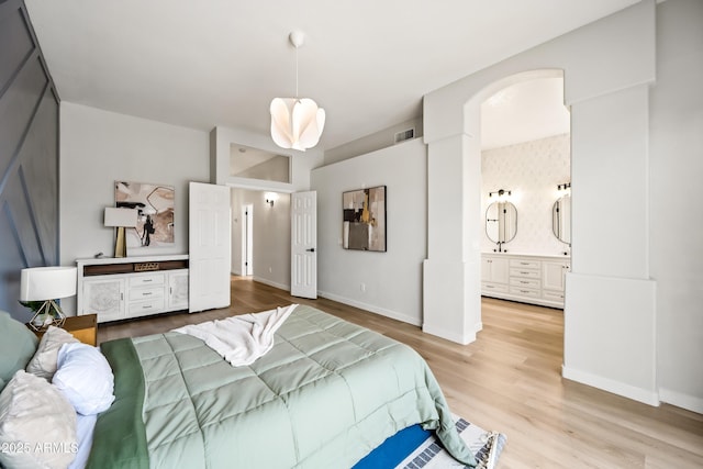 bedroom featuring connected bathroom, visible vents, baseboards, and wood finished floors