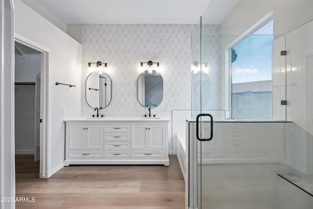 full bathroom with wallpapered walls, a shower stall, wood finished floors, and a sink