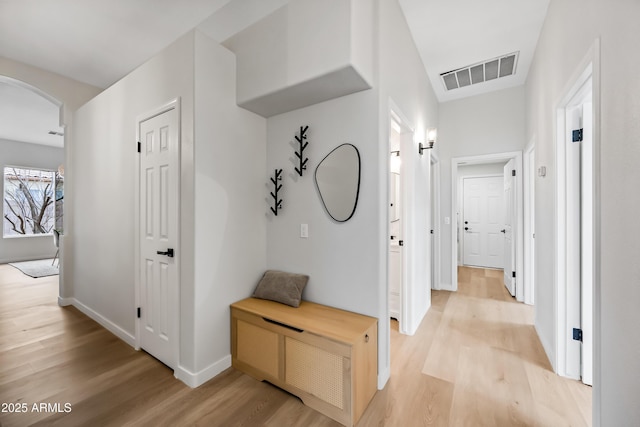 hallway featuring light wood-type flooring, visible vents, arched walkways, and baseboards