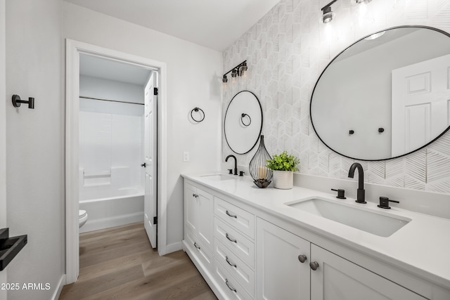 full bath with double vanity, toilet, wood finished floors, and a sink