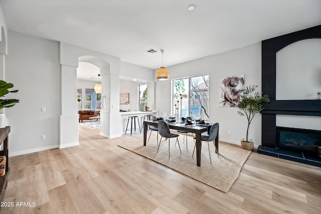 dining room featuring a glass covered fireplace, wood finished floors, arched walkways, and baseboards