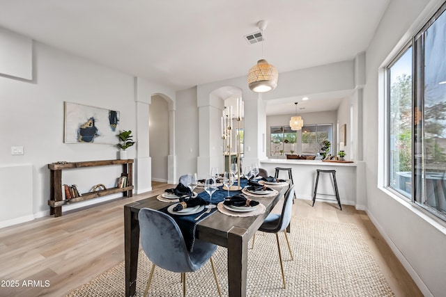 dining area with visible vents, arched walkways, light wood-style floors, and baseboards