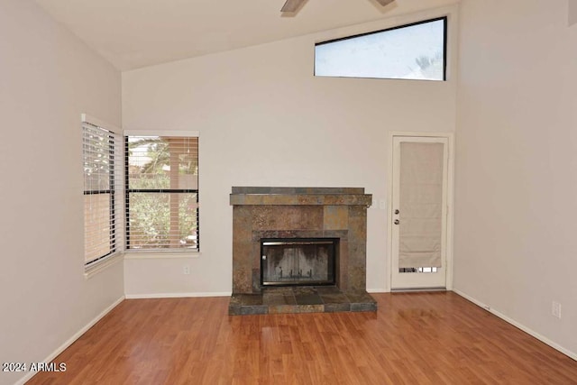 unfurnished living room with hardwood / wood-style flooring, ceiling fan, high vaulted ceiling, and a tile fireplace