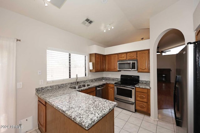 kitchen with light stone countertops, appliances with stainless steel finishes, vaulted ceiling, sink, and light tile patterned floors