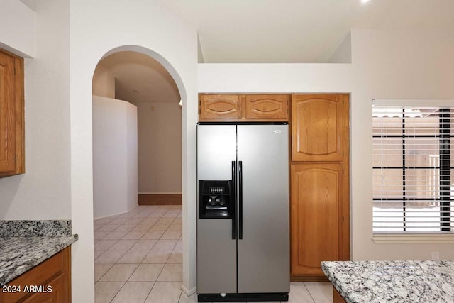 kitchen featuring light stone countertops, light tile patterned floors, and stainless steel refrigerator with ice dispenser