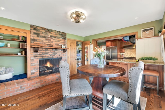 dining room with a brick fireplace and dark hardwood / wood-style floors