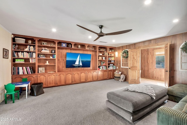 carpeted living room with ceiling fan, built in features, and wood walls