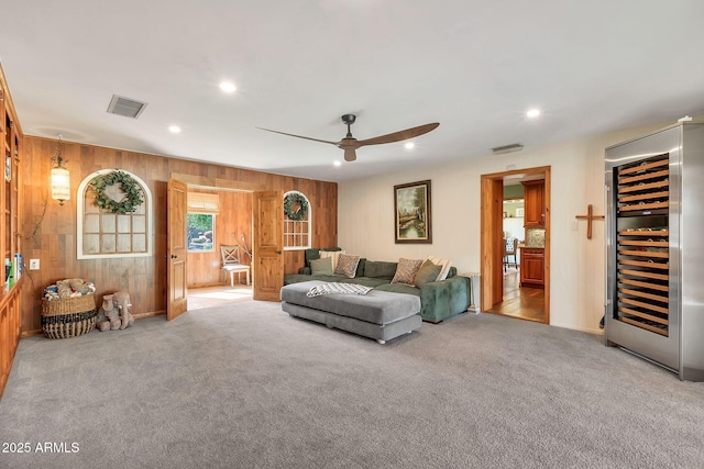 carpeted living room featuring wine cooler, wooden walls, and ceiling fan