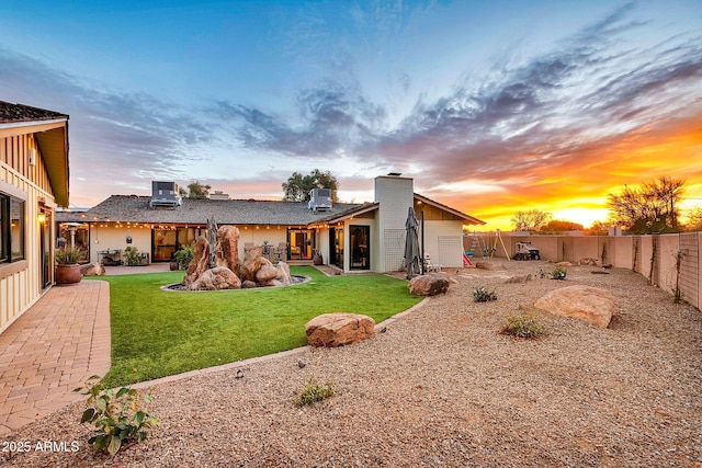 back house at dusk featuring a patio, cooling unit, and a lawn