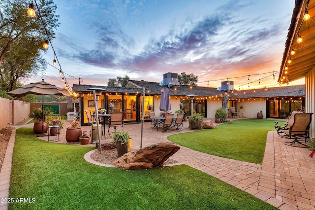 back house at dusk featuring a yard and a patio