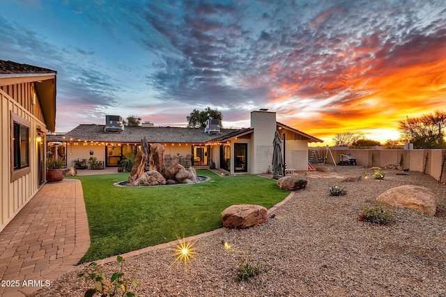 back house at dusk with a patio area and a lawn