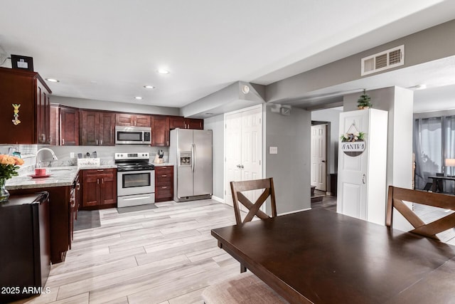 kitchen with appliances with stainless steel finishes, light hardwood / wood-style floors, light stone counters, and sink