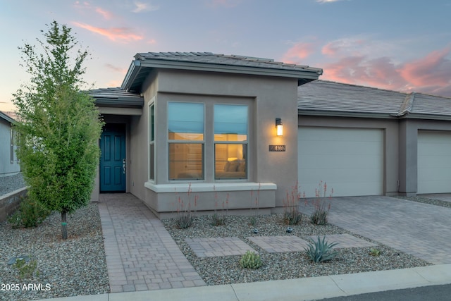 view of front facade featuring a tile roof, an attached garage, driveway, and stucco siding