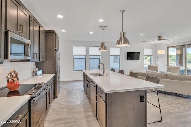 kitchen featuring a kitchen bar, dark brown cabinets, a sink, light countertops, and stainless steel appliances