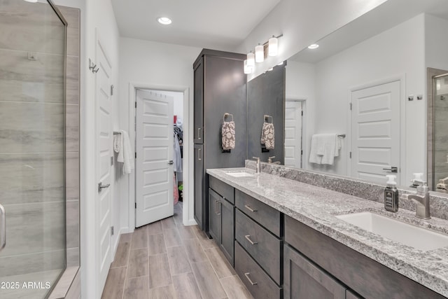 bathroom with a spacious closet, double vanity, a sink, and a stall shower