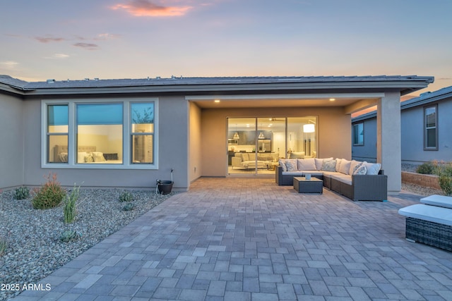 back of property at dusk with an outdoor hangout area, stucco siding, and a patio area