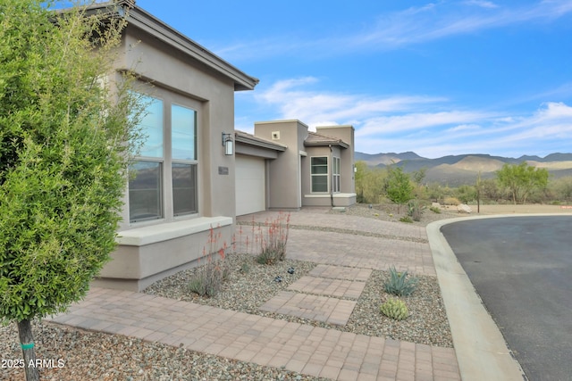view of side of property with a mountain view, driveway, a garage, and stucco siding
