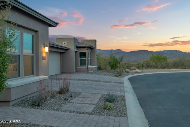 property exterior at dusk with a garage, driveway, a mountain view, and stucco siding