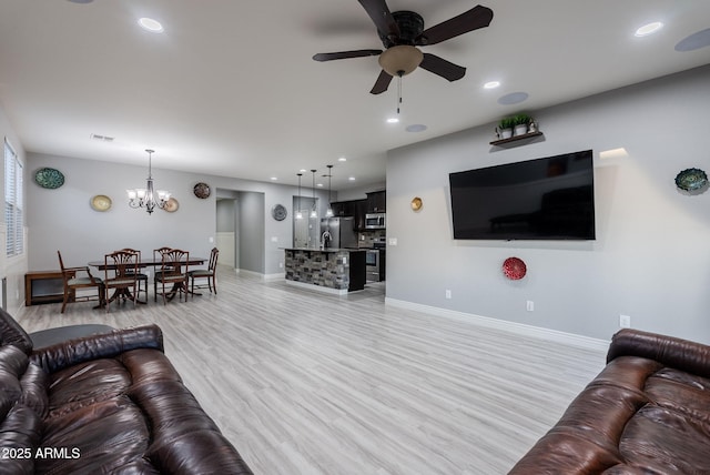 living room featuring ceiling fan with notable chandelier and light hardwood / wood-style floors