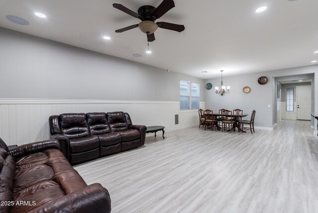 living room featuring ceiling fan with notable chandelier and light hardwood / wood-style flooring