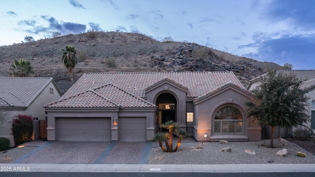 view of front of property with an attached garage, a mountain view, a tile roof, decorative driveway, and stucco siding