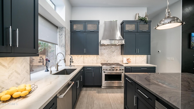 kitchen with tasteful backsplash, wall chimney exhaust hood, light stone countertops, stainless steel appliances, and a sink