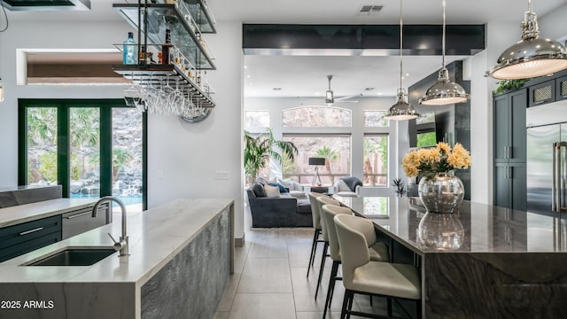 kitchen featuring visible vents, stainless steel built in fridge, a sink, light stone countertops, and a large island with sink