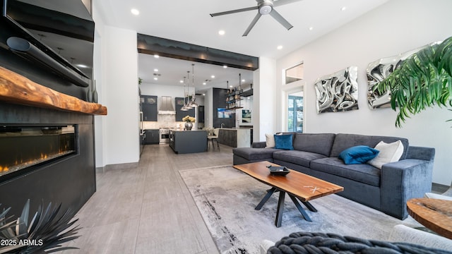 living area featuring a glass covered fireplace, a ceiling fan, and recessed lighting