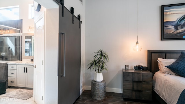 bedroom with wood tiled floor, baseboards, ensuite bath, and a barn door