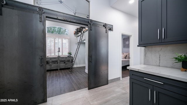 kitchen with a barn door, wood finish floors, baseboards, light stone countertops, and tasteful backsplash