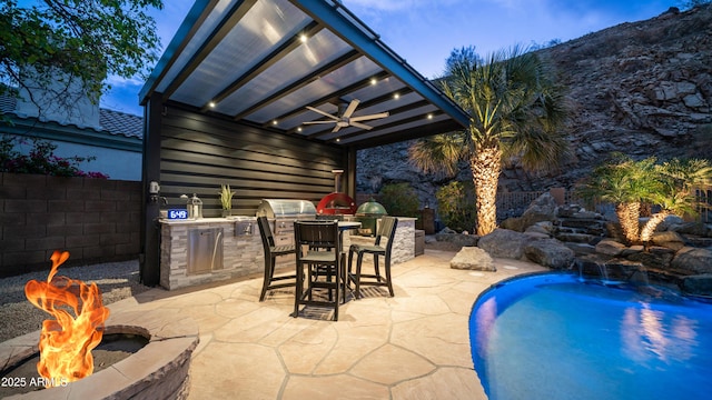 view of patio featuring an outdoor fire pit, exterior kitchen, a ceiling fan, and fence